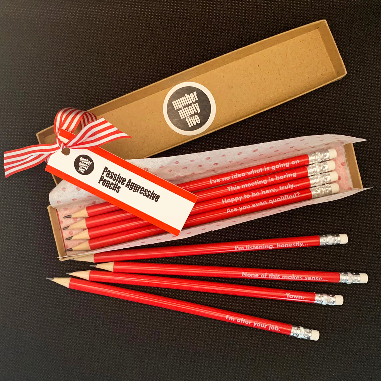 Number Ninety Five, Passive Aggressive pencils, 8 sharpened red pencils with white rubber tips, gift wrapped in a kraft box, with phases such as, I have no idea what is going on, This Meeting is Boring, Are you even qualified? and I'm after your job written on them in white text.