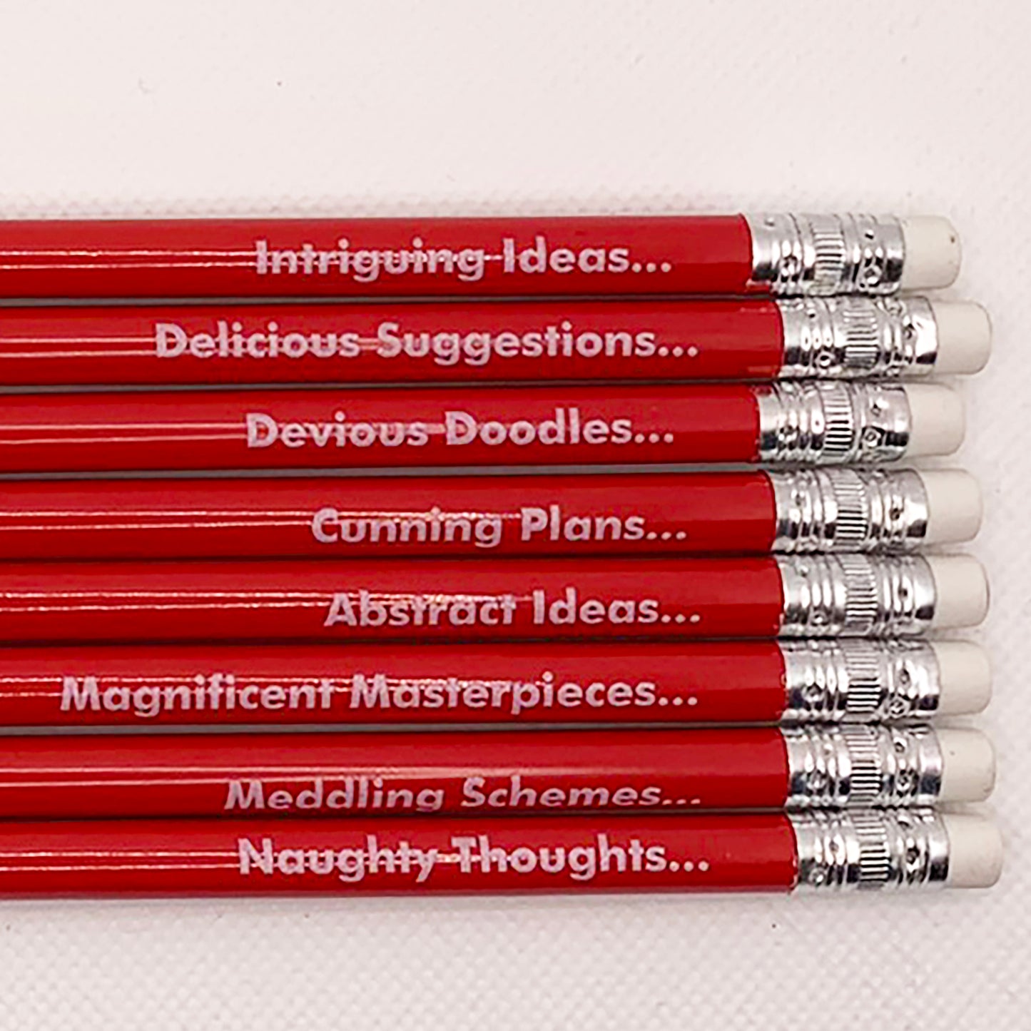 Number Ninety Five, Pencils for Plotting, 8 sharpened red pencils with white rubber tips, with phases such as, Magnificent Masterpieces, Abstract Ideas, Cunning Plans and Delicious Suggestions written on them in white text.