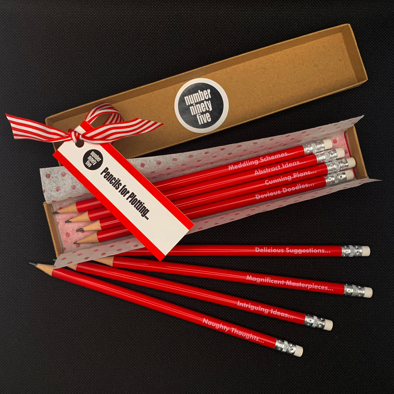 Number Ninety Five, Pencils for Plotting, 8 sharpened red pencils with white rubber tips, gift wrapped in a kraft box, with phases such as, Magnificent Masterpieces, Abstract Ideas, Cunning Plans and Delicious Suggestions written on them in white text.